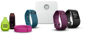 Several types of FitBit (fitness activity tracker) devices, such as a watch and a belt clip, lined up.